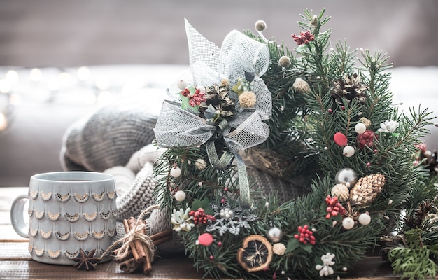 Christmas still life of Christmas trees and decorations, festive wreath on a background of knitted clothes and beautiful cups, Christmas spices