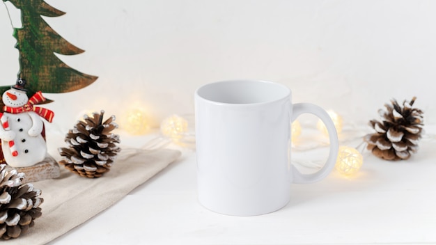 Christmas table composition. Cup of tea, fir cones and decoration. White wall