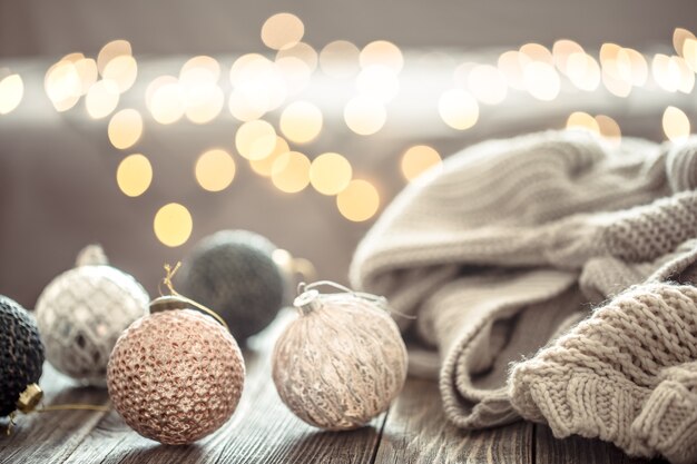 Christmas tree decorations over Christmas lights bokeh in home on wooden table with sweater on a wall and decorations.