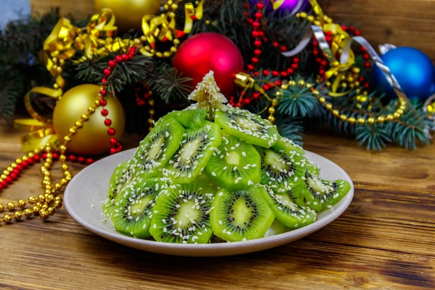 나무 테이블에 크리스마스 트리 모양의 과일 샐러드와 크리스마스 장식이 있습니다. 크리스마스와 새해 축제 디저트를 위한 창의적인 아이디어. 아이들을 위한 재미있는 음식 아이디어