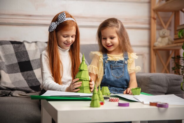 Christmas tree. Two little children, girls together in creativity. Happy kids make handmade toys for games or New Year celebration. Little caucasian models. Happy childhood, Celebration preparation.