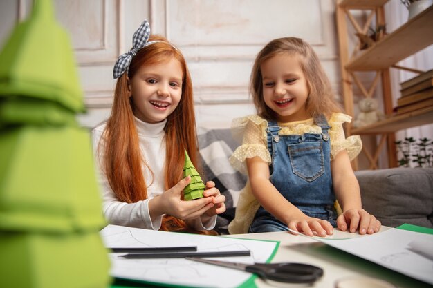 Christmas tree. Two little children, girls together in creativity. Happy kids make handmade toys for games or New Year celebration. Little caucasian models. Happy childhood, Celebration preparation.