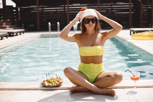 Christmas woman relaxing by the swimming pool. Funny girl celebrating Christmas in a resort. With cocktail and fruits.