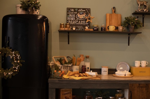 Christmas wreath and fir tree branches in vases and cups all around the modern kitchen. Modern kitchen with black fridge decorated for Christmas and New Year.