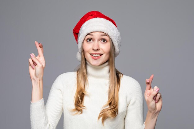 Christmayoung woman prays on Santa hat isolated on a gray wall