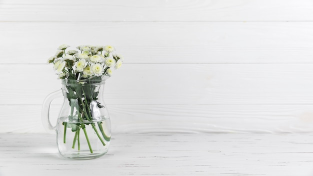 Chrysanthemum flowers inside the glass jug against white wooden background