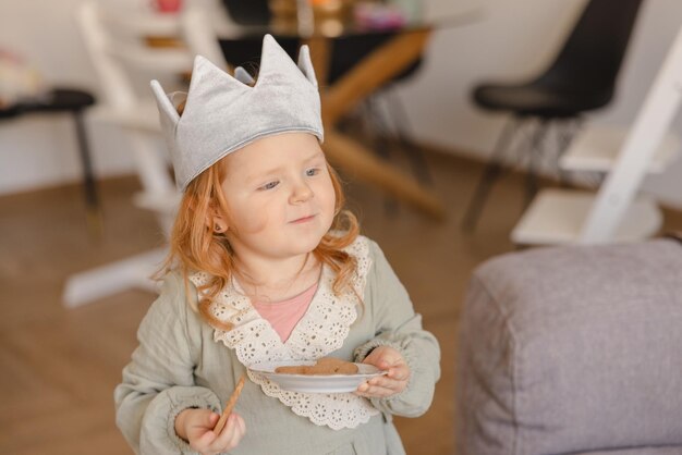 ドレスの赤い髪のぽっちゃり白人の小さな女の子の子供は、部屋にクッキーのプレートを保持します離乳食の概念