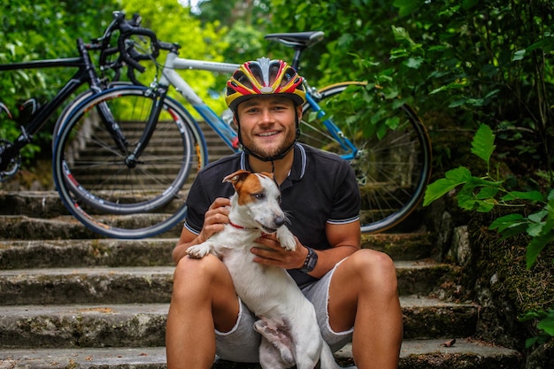 Foto gratuita ciclista maschio in posa con il suo cane russel sulle scale in una foresta.