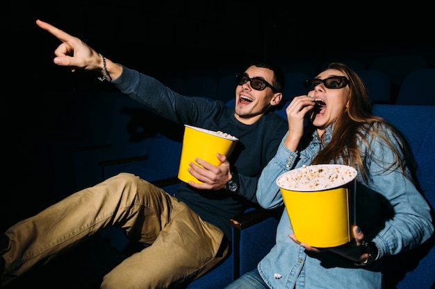Free photo cinema day, young couple with popcorn looking action movie in cinema.