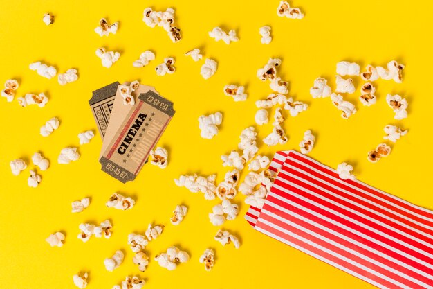 Cinema tickets over the spilled popcorns against yellow backdrop