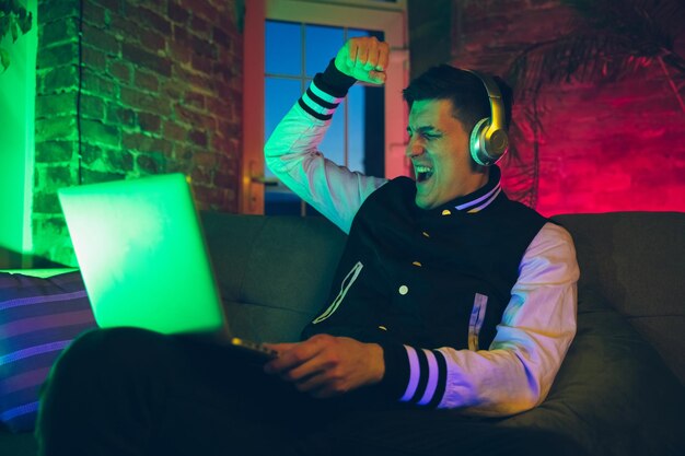 Cinematic portrait of handsome young man using devices, gadgets in neon lighted interior