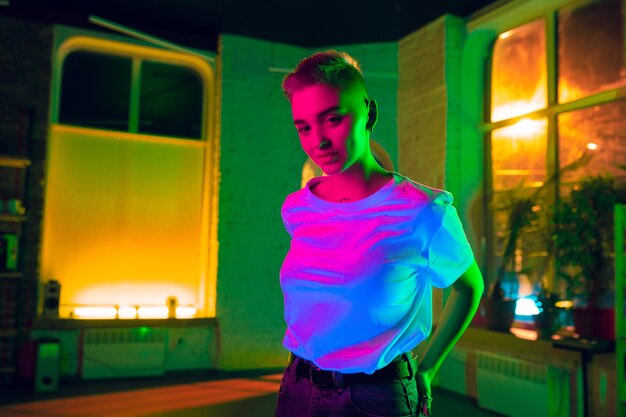 Cinematic portrait of stylish woman in neon lighted interior. Toned like cinema effects, bright neoned colors. Caucasian model posing confident in colorful lights indoors. Youth culture.