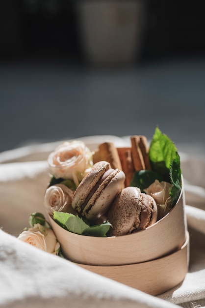 Cinnamon macaroons with pink roses in wooden container over the clothes