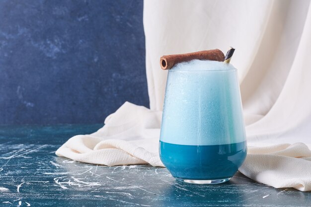 Cinnamon stick with a cup of drink on blue.