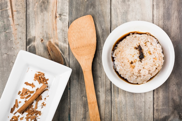 Cinnamon sticks in white tray with soya sauce rice and spatula on wooden table