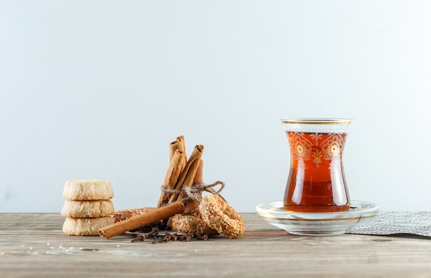 Cinnamon sticks with biscuits, cloves, a glass of tea, placemat side view on wooden and white wall