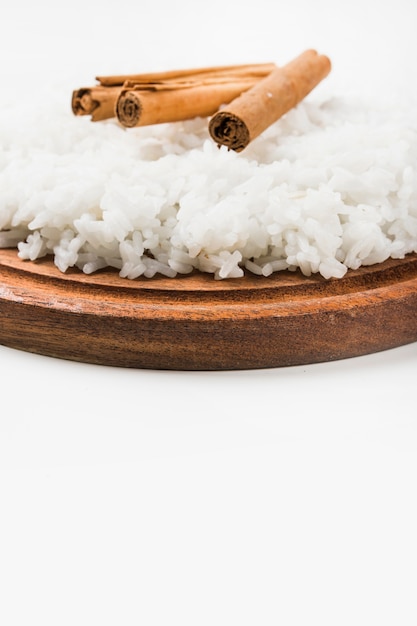 Cinnamon sticks with cooked rice over wooden plate against white background