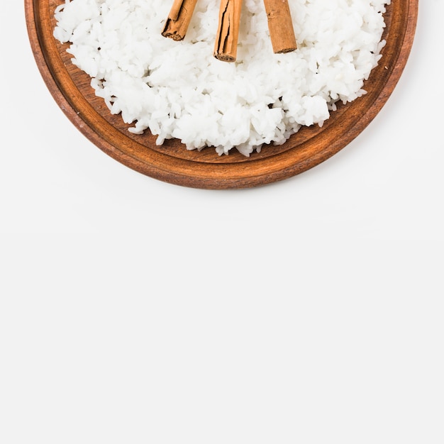 Cinnamon sticks with cooked rice over wooden plate against white background