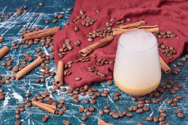 Cinnamons and coffee beans with a cup of drink on blue.