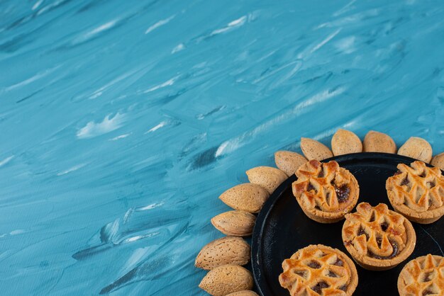 Circle of almonds in shell with sweet fresh round cookies on a blue background. 