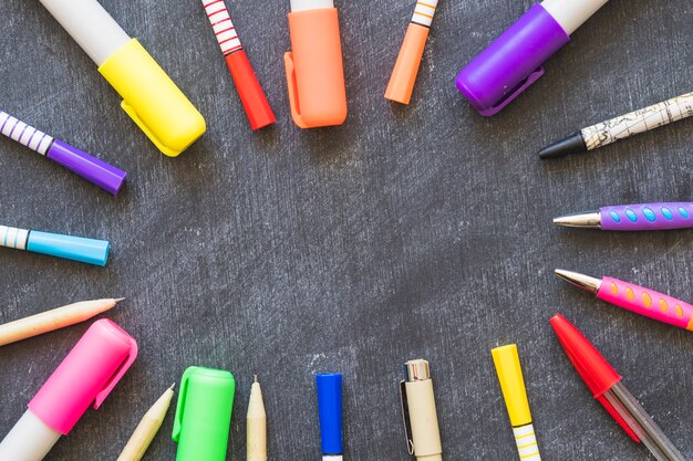 Circle of markers and pens on blackboard background 