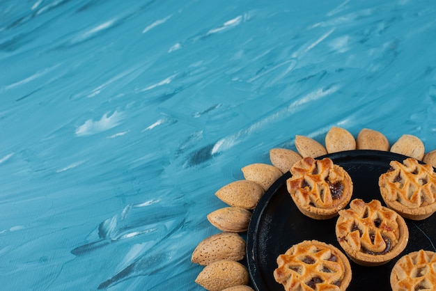 Бесплатное фото Круг миндаля в оболочке со сладким свежим круглым печеньем на синем фоне.