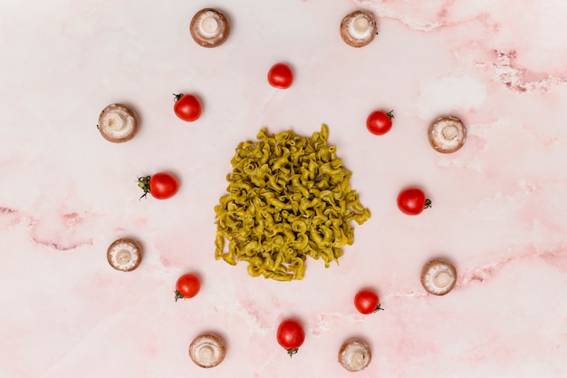 Круговое расположение зеленой сырой пасты; красные помидоры; и гриб на мраморной поверхности