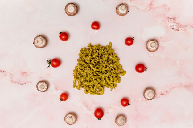 Circular arrangement of green raw pasta; red tomatoes; and mushroom on marble surface