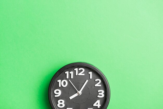 Круглые черные часы на фоне зеленой стены