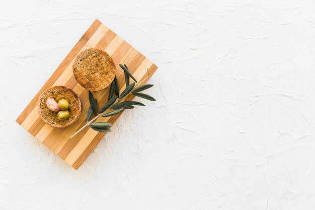 Circular bread with olives and garlic clove with twig on chopping board