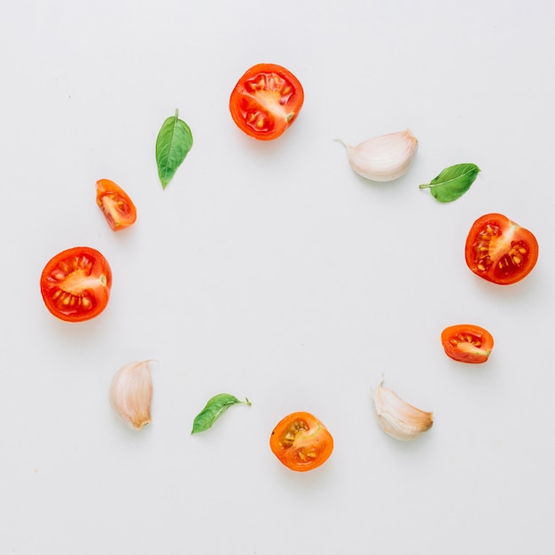 Circular frame made with cherry tomatoes; basil and garlic cloves on white background