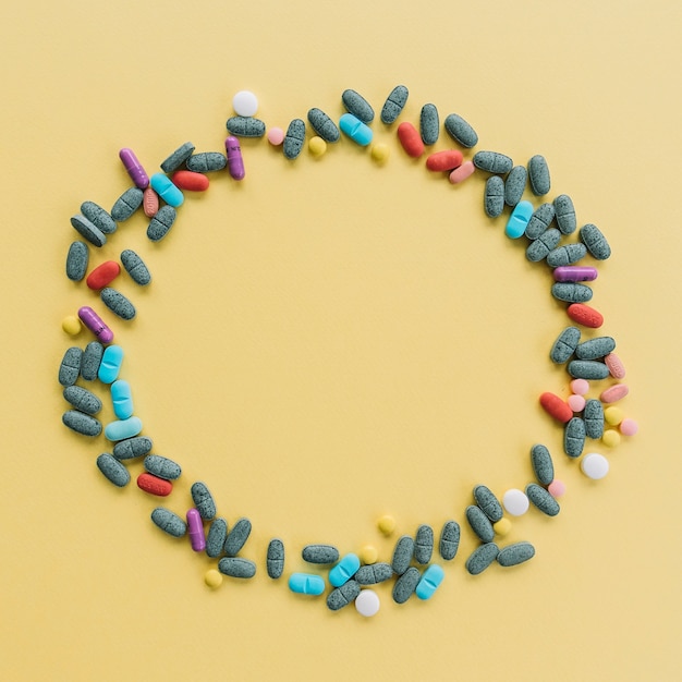 Free photo circular frame made with colorful pills on yellow background