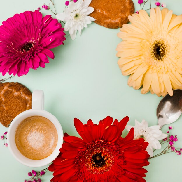 Круглая рамка с цветком гербера; чашка кофе; ложка и печенье на цветном фоне
