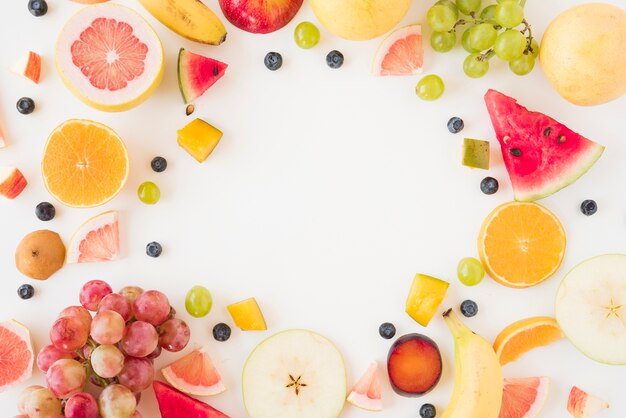 Circular frame made with many organic fruits on white backdrop