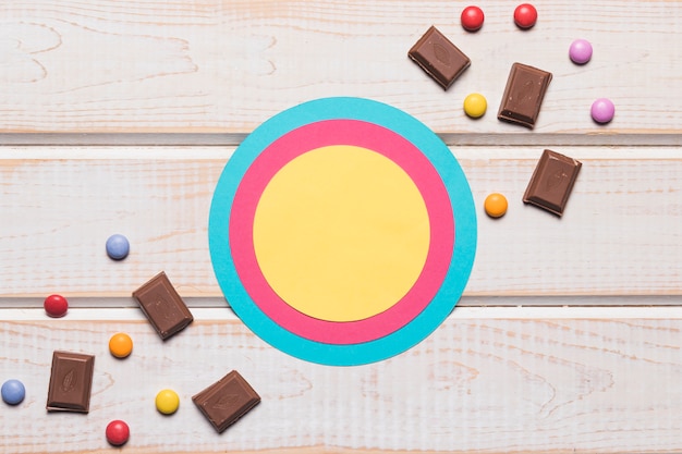 Circular frame with chocolate pieces and gems candies on wooden backdrop