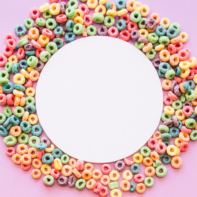 Circular white blank frame decorated with colorful cereal loop rings on pink background