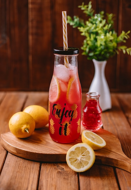 Citrus cocktail with lemon slices and red syrup in bottle with straw pipe