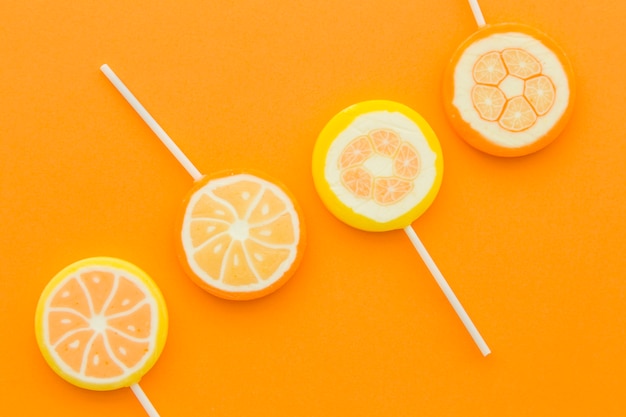 Citrus fruit lollipops in a row on orange backdrop