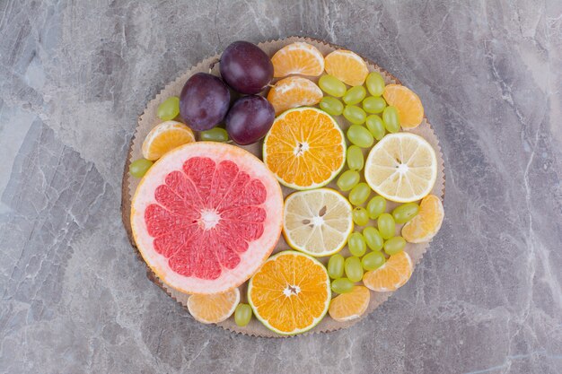 Citrus fruits, plums and grapes on wood piece. 