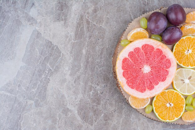 Citrus fruits, plums and grapes on wood piece. 