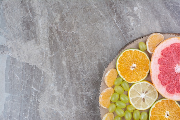 Citrus fruits slices and grapes on wood piece. 