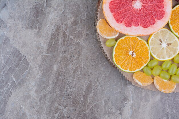 Citrus fruits slices and grapes on wood piece. 