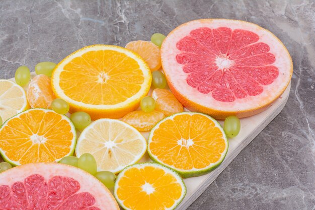 Citrus fruits slices and grapes on wooden board. 