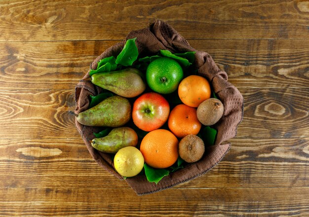 Citrus fruits with apples, pear, kiwi, leaves on wooden table, top view.