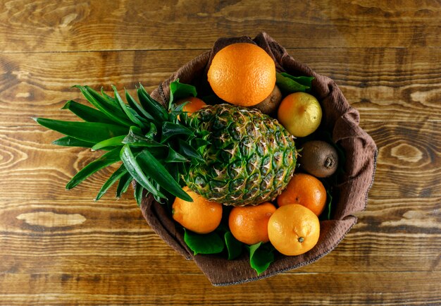 Citrus fruits with kiwi, pineapple, leaves on wooden and kitchen towel, top view.