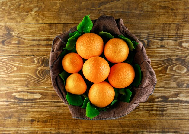 Citrus fruits with leaves on wooden and kitchen towel, top view.