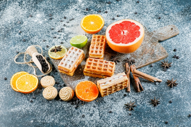 Citrus fruits with waffle, spices, cookies, chocolate chips flat lay on grungy and cutting board table