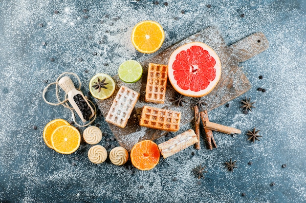 Citrus fruits with waffle, spices, cookies, chocolate chips top view on grungy and cutting board