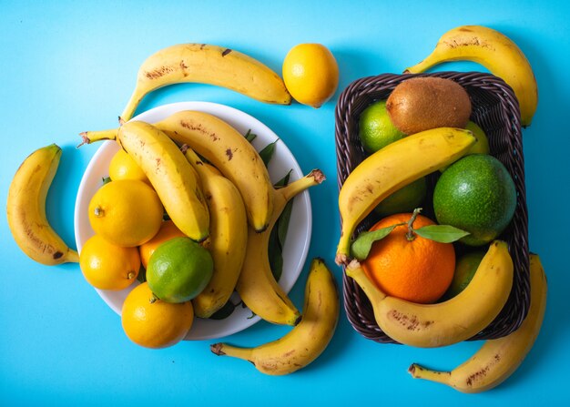 Citrus fruitsavocado bananas lemon kiwi orange in plate and basket on blue surface