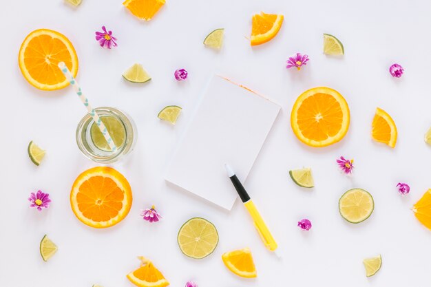 Citruses and and flowers around drink and notebook